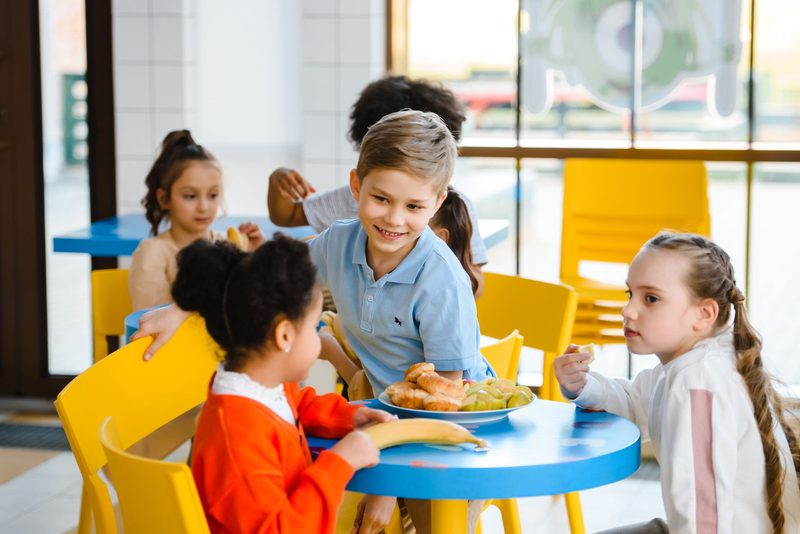 Kinder essen lachend gemeinsam an einem blauen Tisch