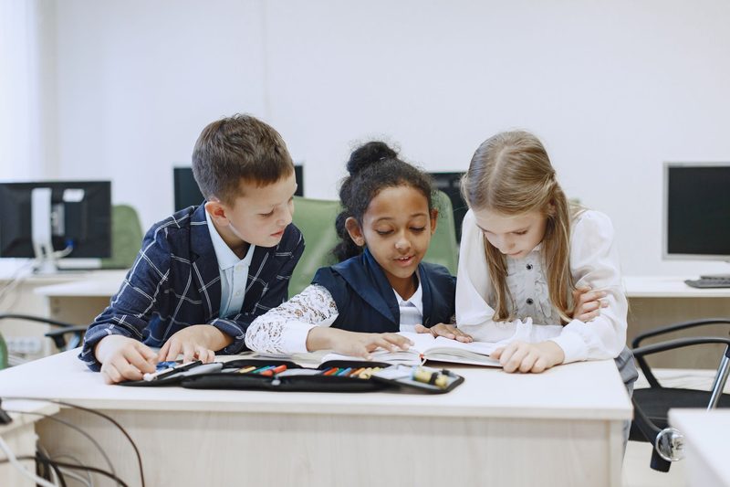 Drei Kinder arbeiten an einem Tisch zusammen an einem Buch
