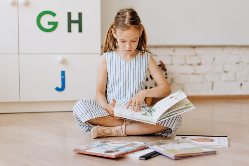 Ein Mädchen sitzt auf dem Boden und liest Bilderbücher