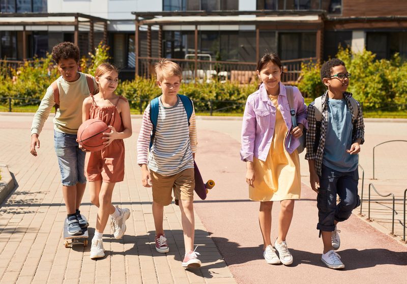 Eine Gruppe Kinder mit Rucksäcken geht über den Schulhof