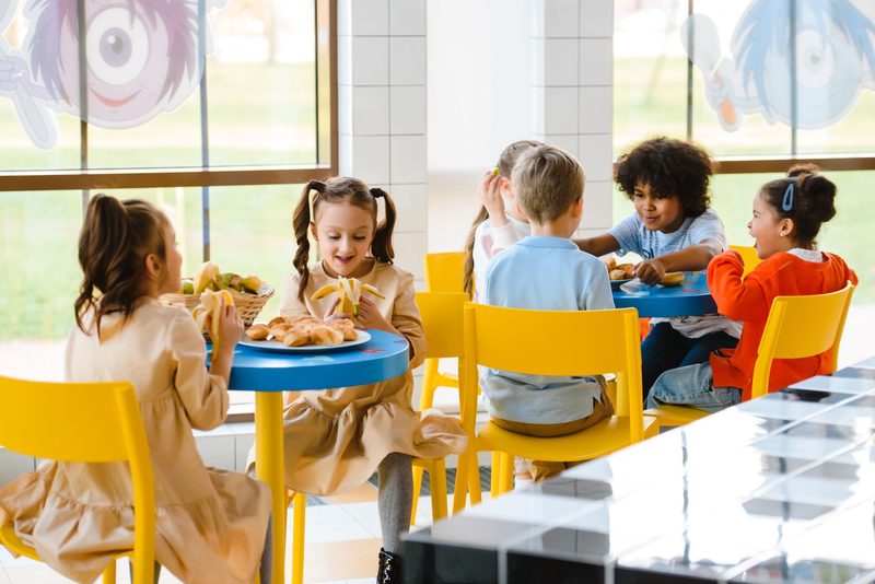 Kinder essen gemeinsam an einem Tisch mit gelben Stühlen
